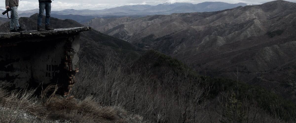 Two people standing on a cliff overlooking a mountainous landscape.
