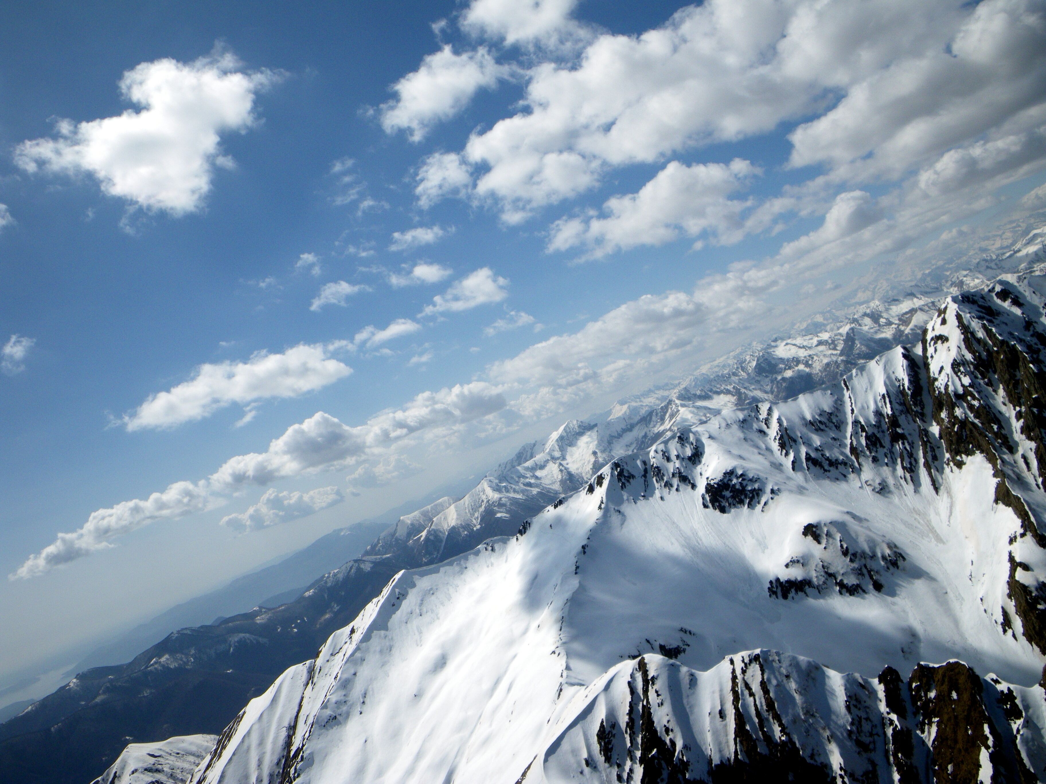 A snow-covered mountain range under a partly cloudy sky.