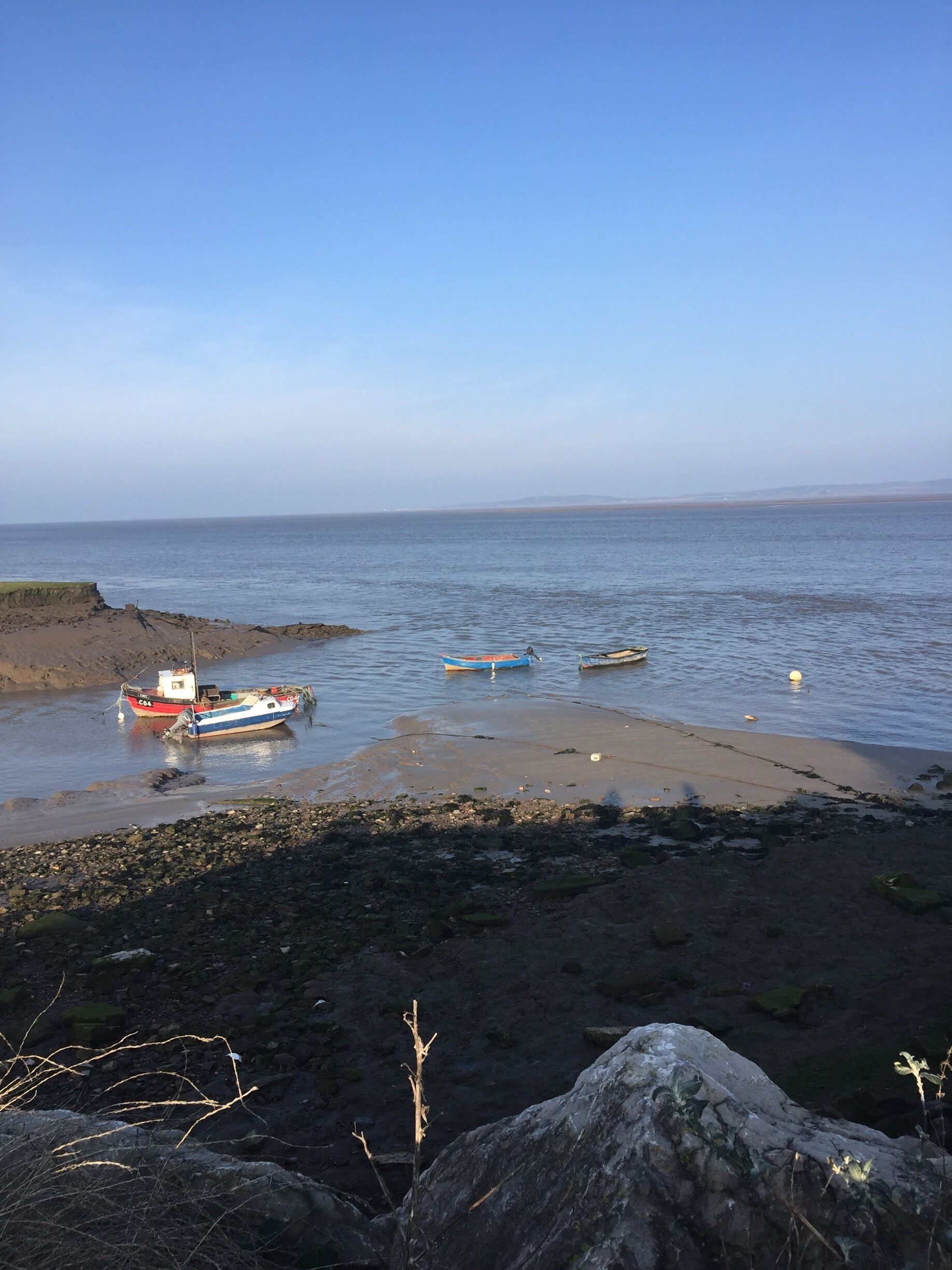A rocky shoreline with several boats anchored near the water's edge.