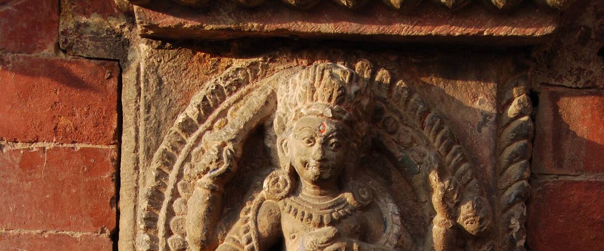A stone carving of a deity with a lion, set against a brick wall.