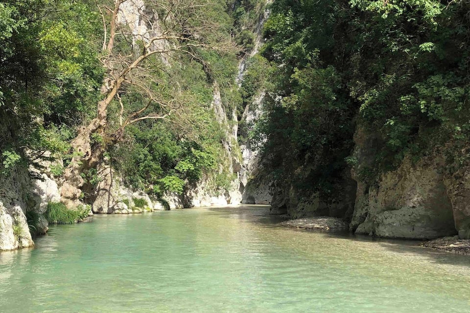 A clear river surrounded by rocky cliffs and dense greenery.