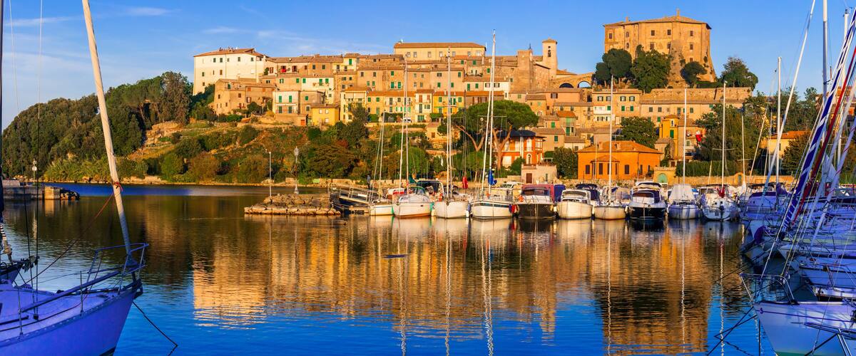 A harbor with boats and a historic building complex on a hill.