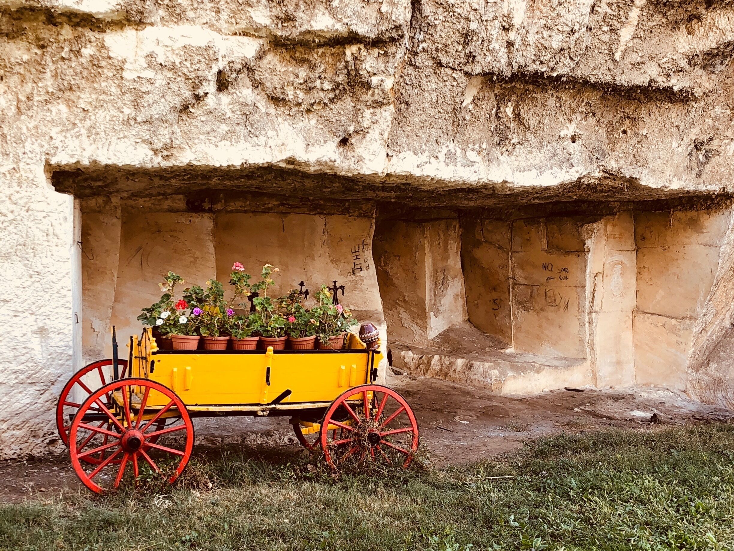 A yellow cart with red wheels parked against a stone wall with graffiti.