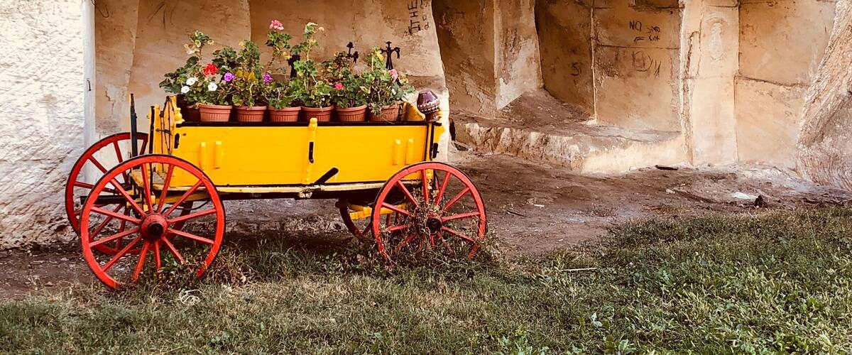 A yellow cart with red wheels parked against a stone wall with graffiti.