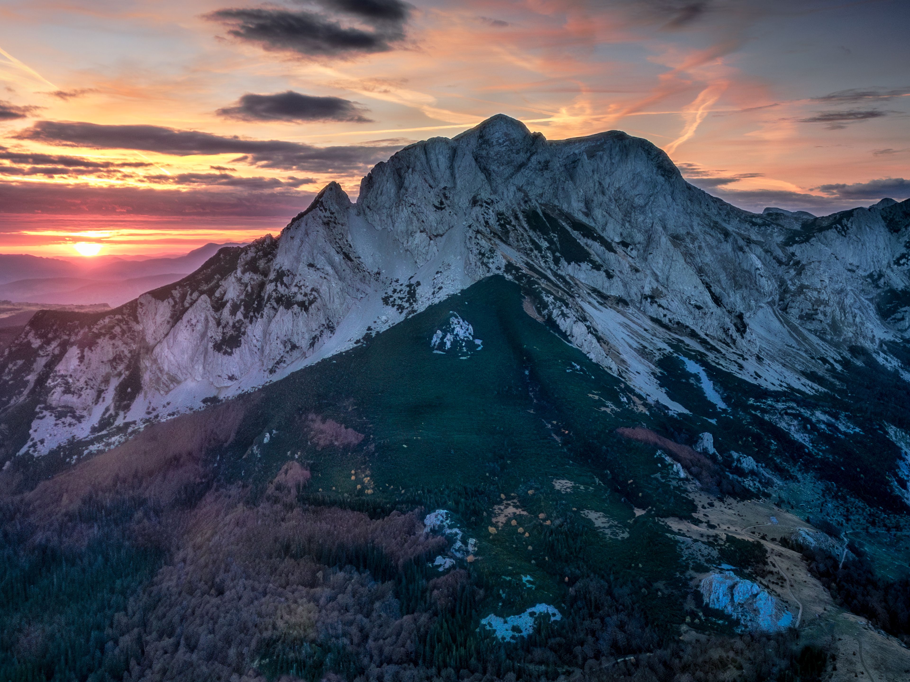Une chaîne de montagnes avec un sommet imposant, une vallée à la végétation clairsemée et un coucher de soleil en arrière-plan.