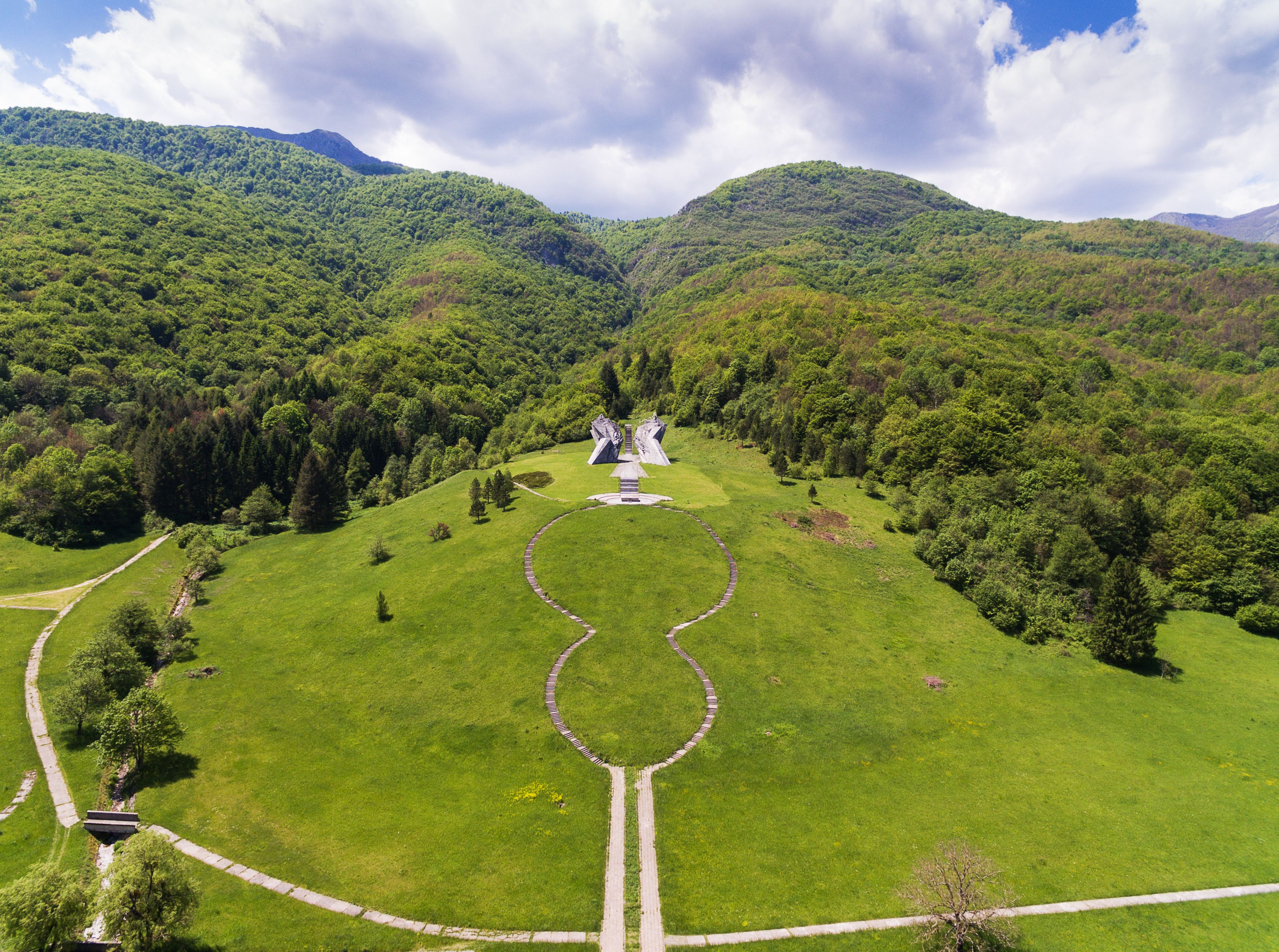 Un paysage verdoyant et luxuriant, avec un imposant bâtiment blanc au centre, entouré d’une forêt dense et de collines ondulantes.