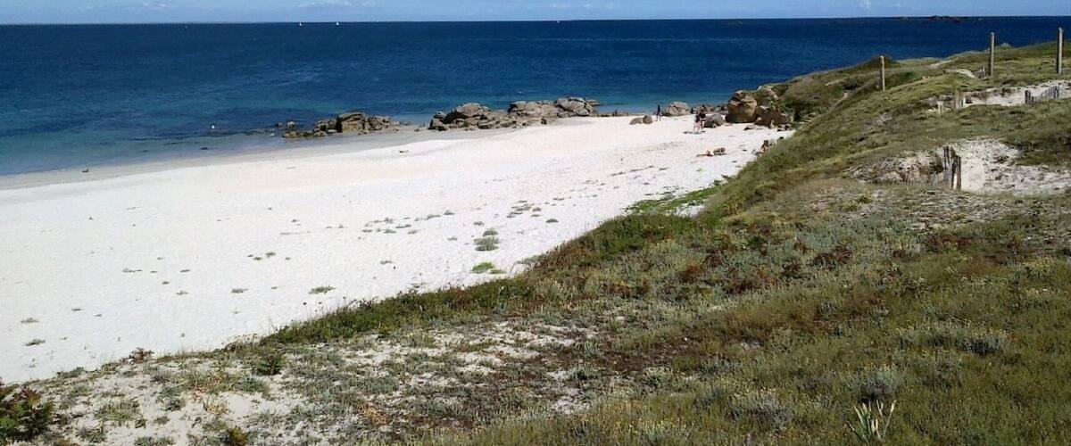 A beach with white sand, a rocky shoreline, and a clear blue sky.