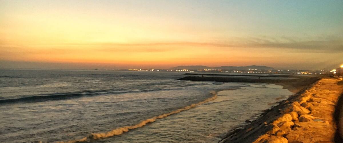 A coastal sunset with waves crashing against a stone wall.
