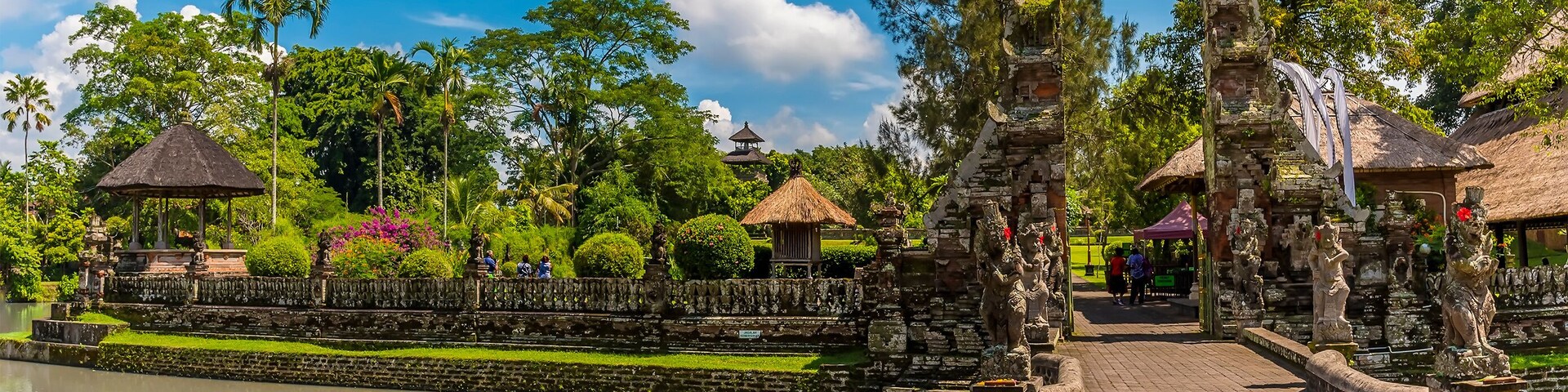 Un complejo de templos sereno con un estanque, estatuas de piedra y abundante vegetación.