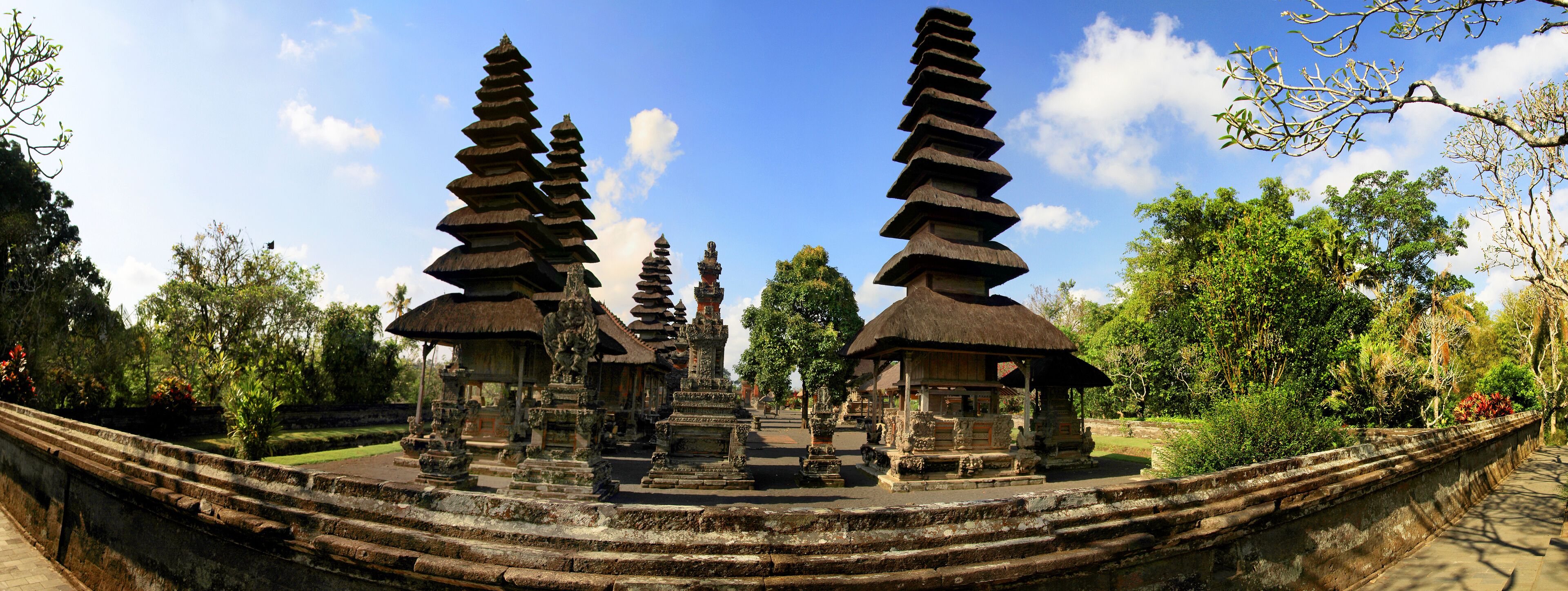 A temple complex with tiered stone structures and thatched-roof buildings.