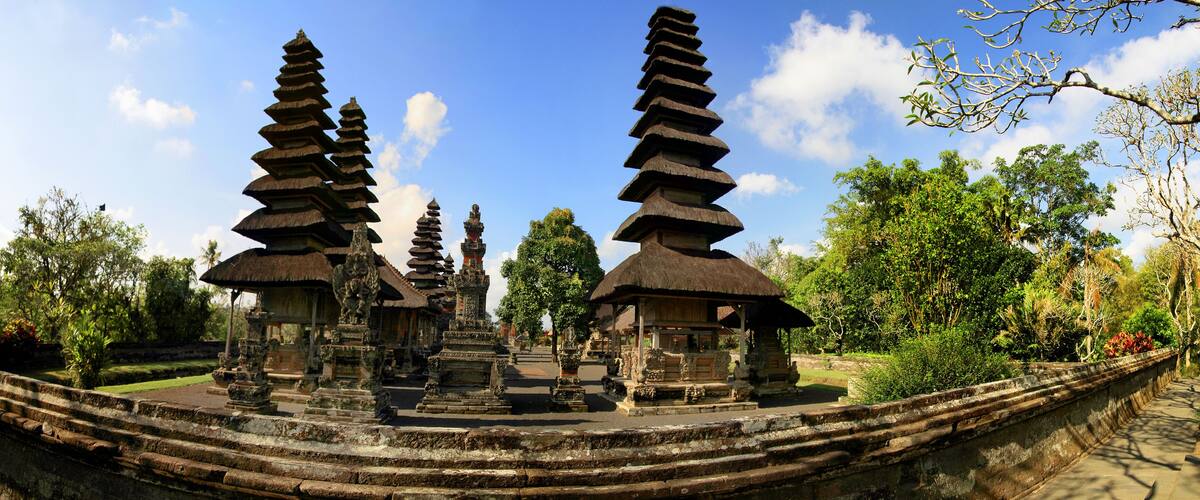 A temple complex with tiered stone structures and thatched-roof buildings.
