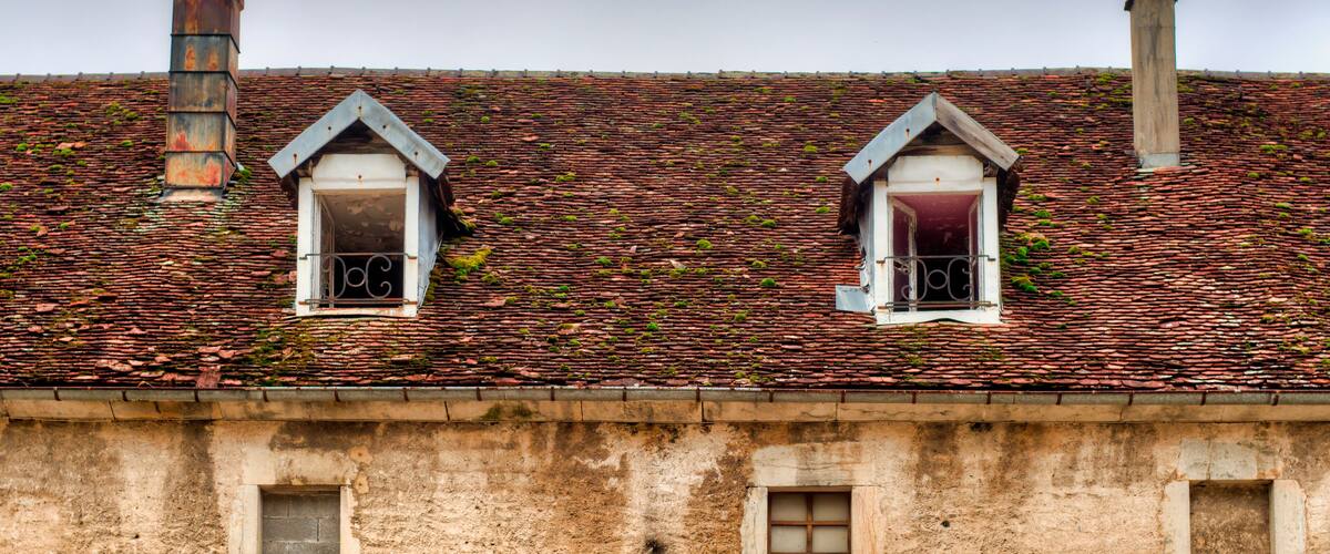 A building with a red-tiled roof and two small windows with metal bars.