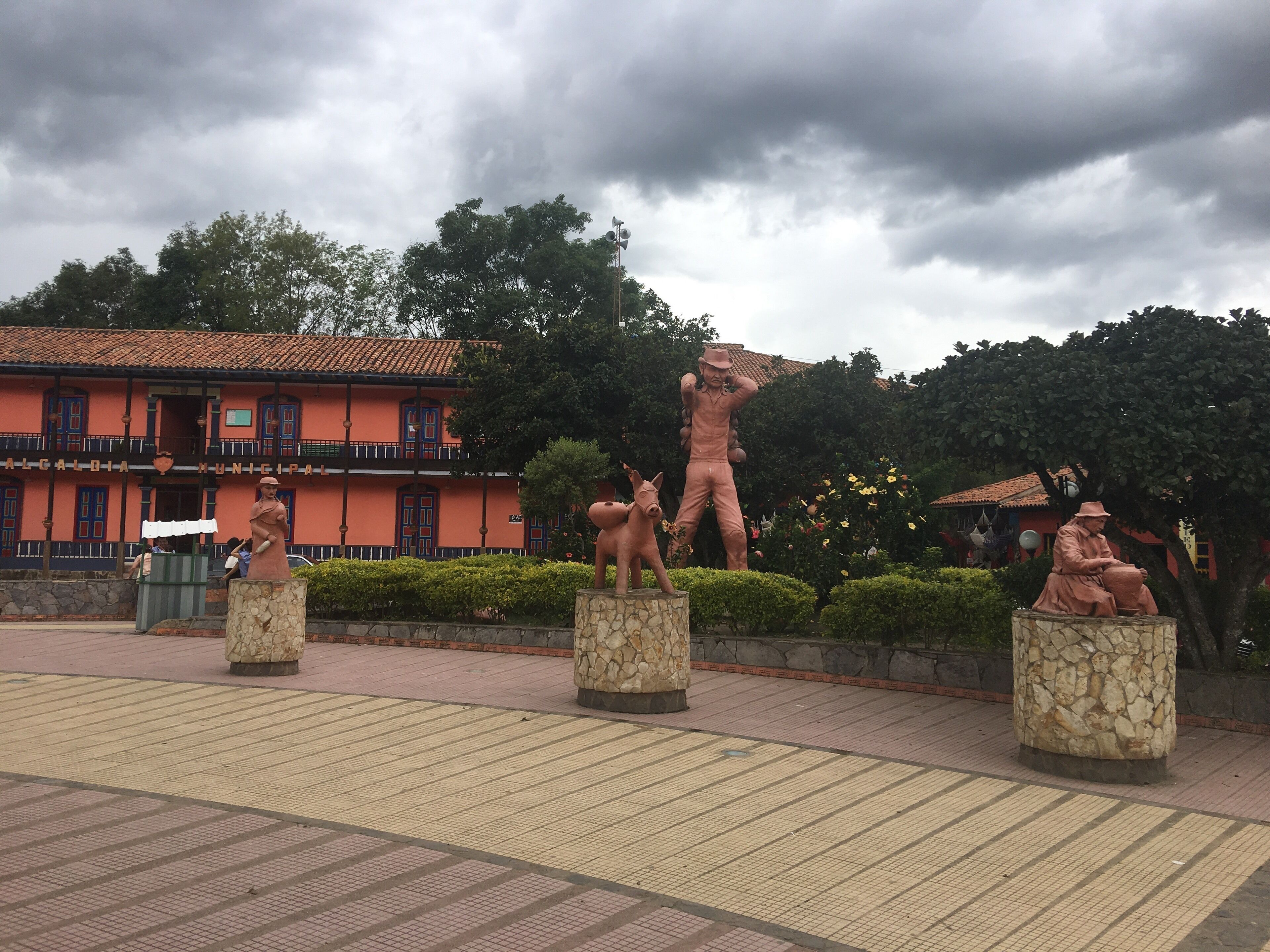 A plaza with statues of a man and a horse, a building with a red facade, and a cloudy sky.