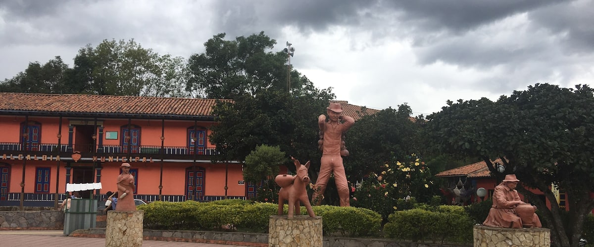 A plaza with statues of a man and a horse, a building with a red facade, and a cloudy sky.