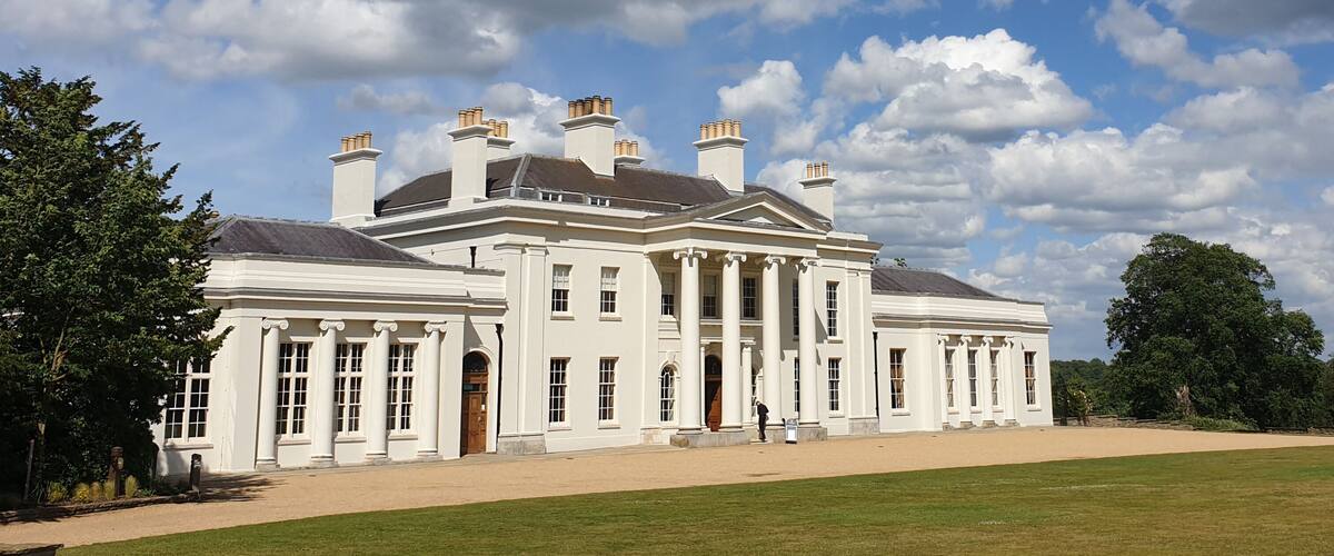 A large white mansion with multiple chimneys and columns, surrounded by a well-maintained lawn and trees.