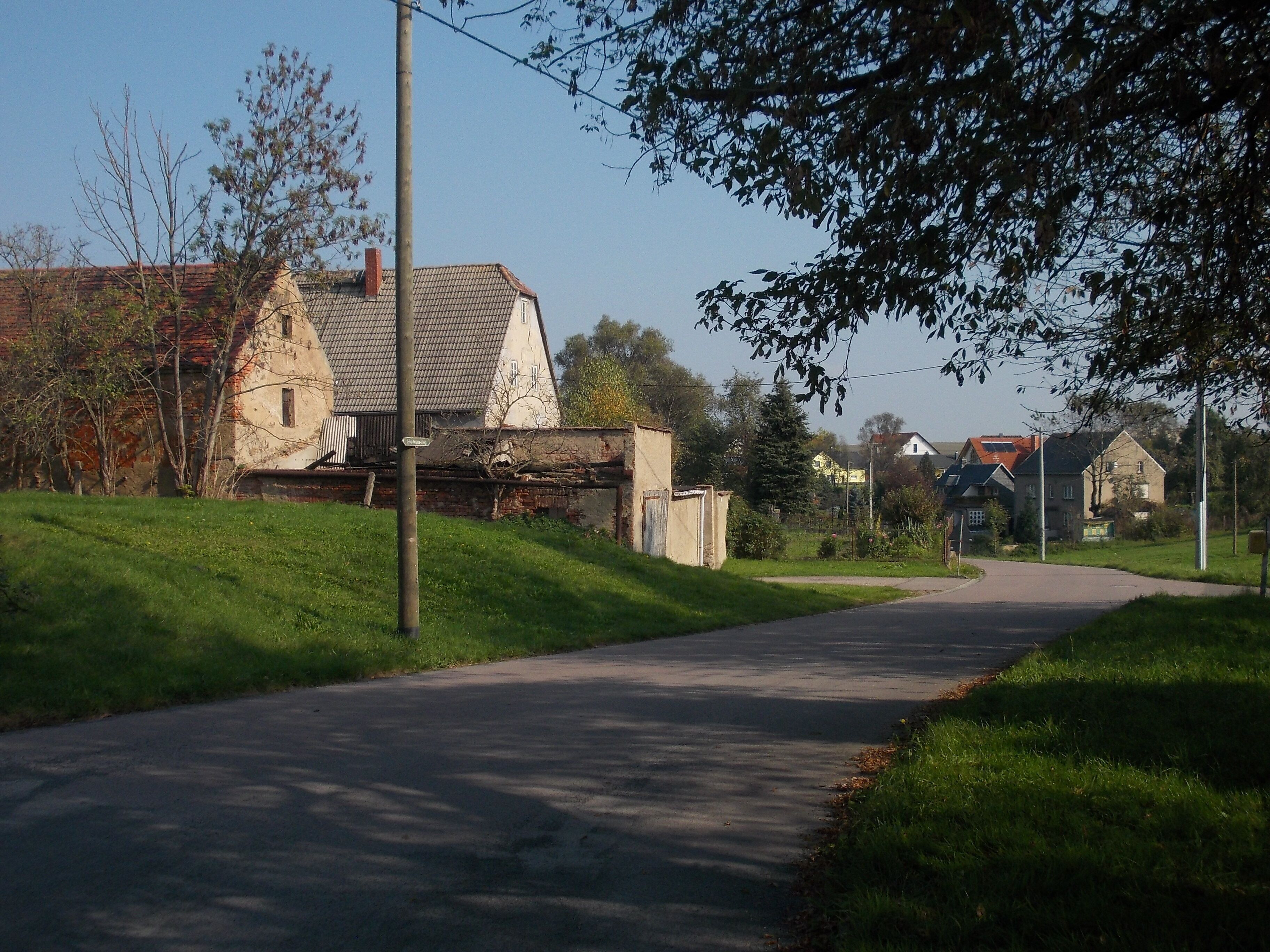 A rural road flanked by houses with red-tiled roofs and a grassy area.