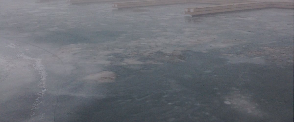 A foggy waterfront with docks and a frozen surface.