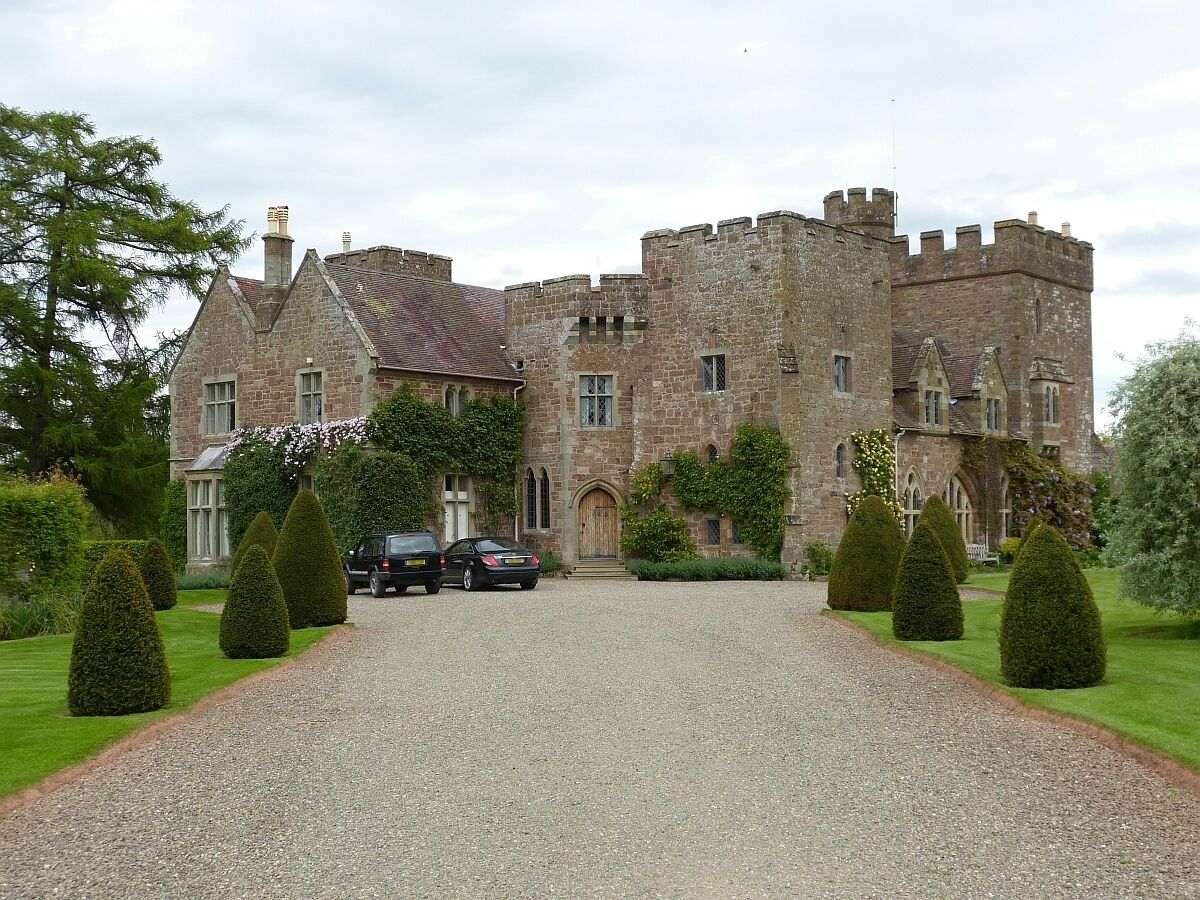 A historic stone castle with a gravel driveway and neatly trimmed hedges.