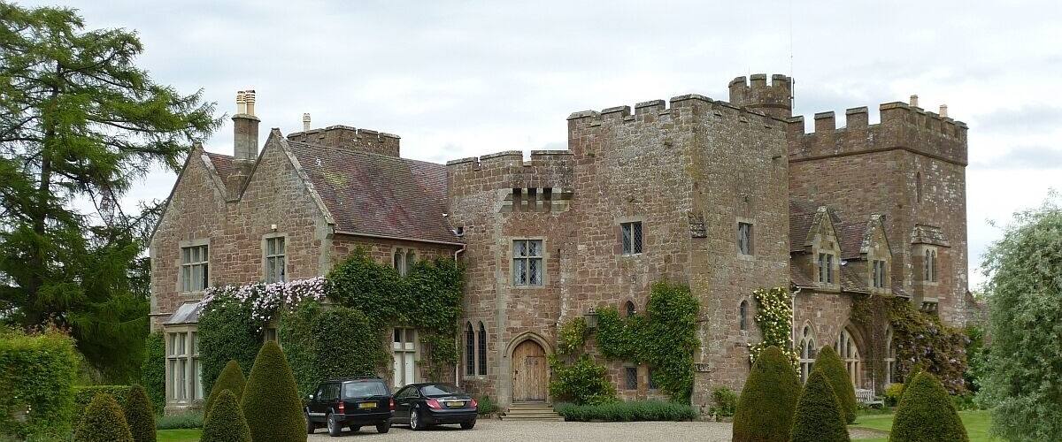 A historic stone castle with a gravel driveway and neatly trimmed hedges.