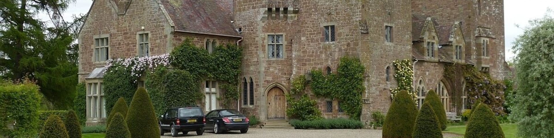 A historic stone castle with a gravel driveway and neatly trimmed hedges.