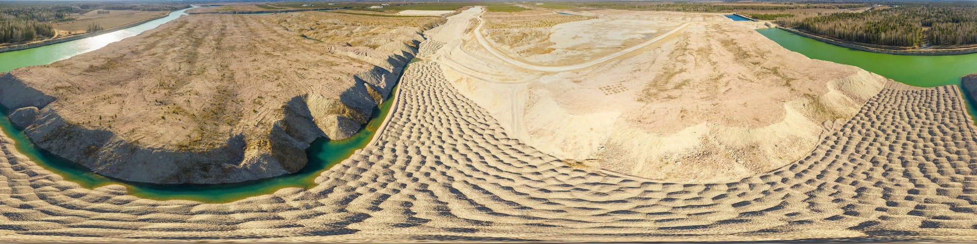 An aerial view of a mining area with a river and forested areas in the background.