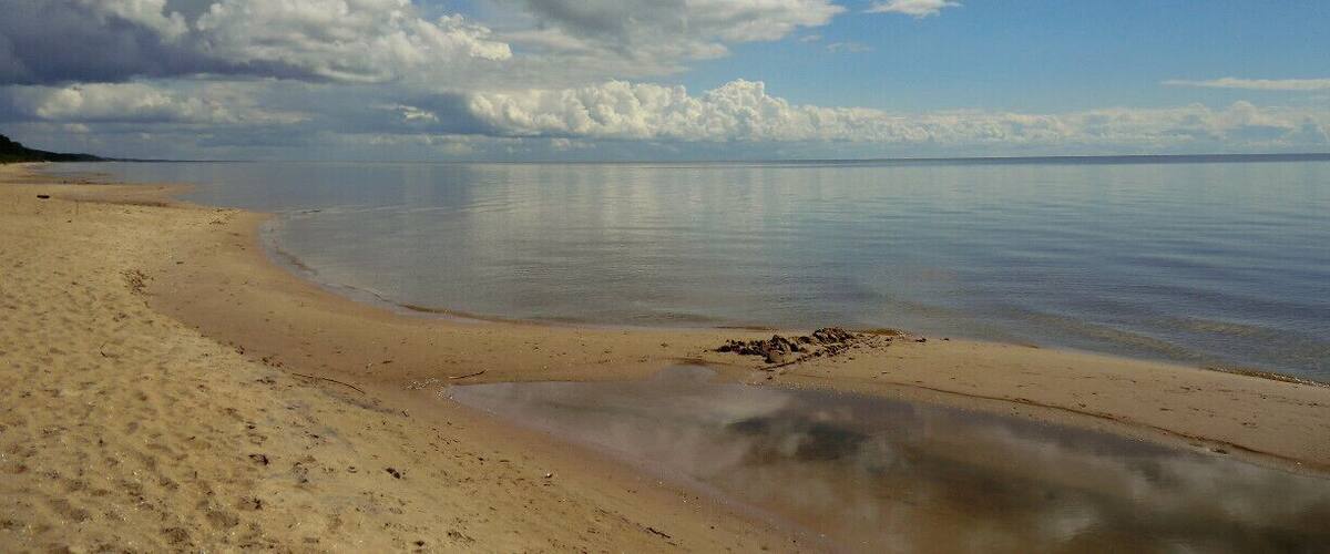 A beach with a sandy shore and calm water under a partly cloudy sky.