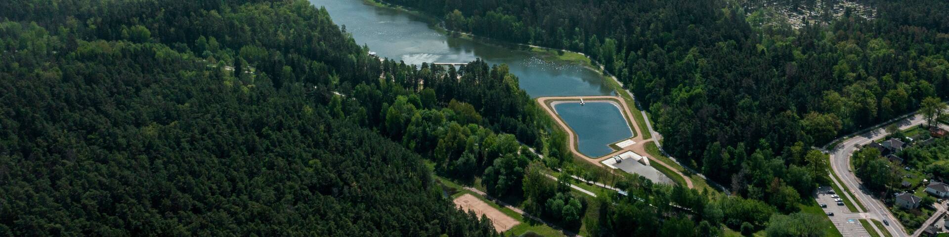 A lake surrounded by dense forest, a small park, and a road with buildings.