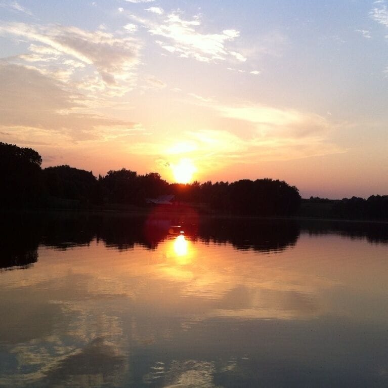 Un atardecer sobre un lago tranquilo con siluetas de árboles contra el cielo.