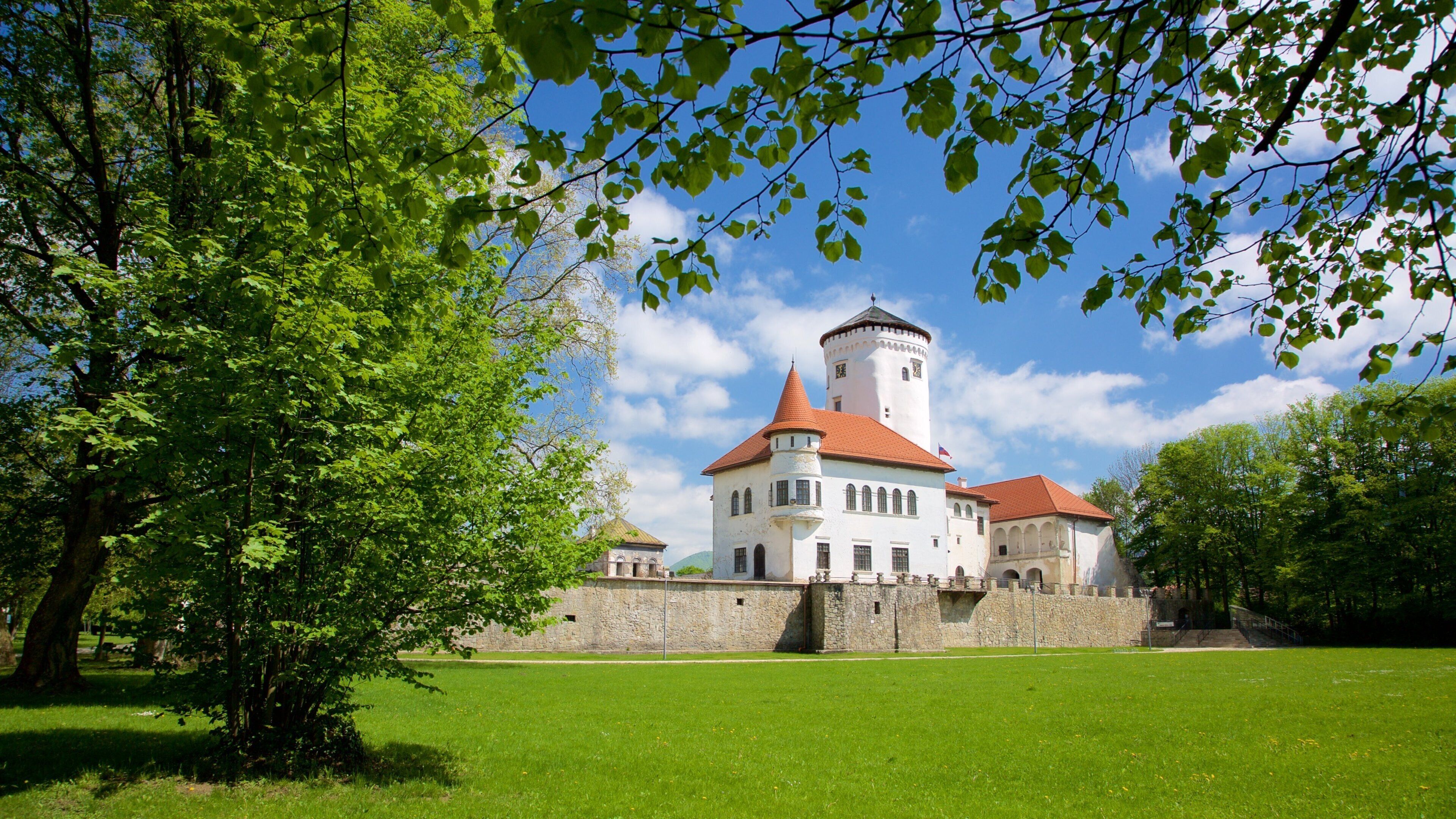 A castle with a red-tiled roof, surrounded by a stone wall and lush green trees.
