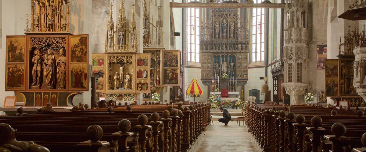 An ornate church interior with rows of wooden pews, religious paintings, and a large altar.