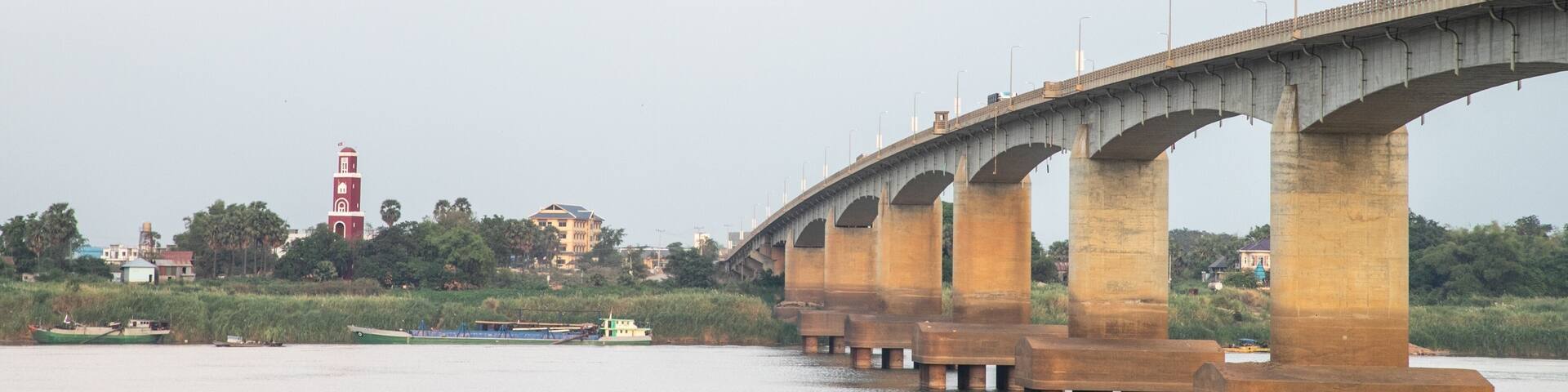 A large concrete bridge spanning a river with multiple arches, a lighthouse, and buildings in the background.