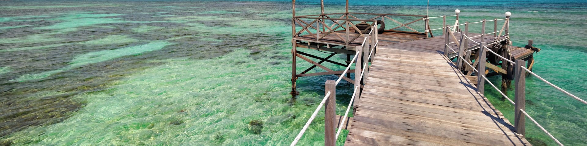 A rustic wooden pier extends into the ocean on Mantanani Island, Borneo.
