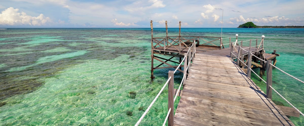 A wooden pier extending into clear turquoise waters with a distant island.