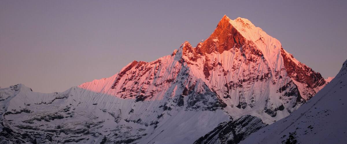 A snow-covered mountain peak with a reddish glow at its summit, surrounded by snow-covered slopes.