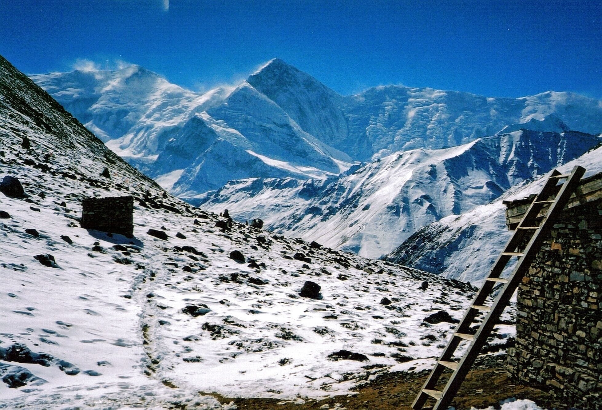 A snow-covered mountain landscape with a stone wall and a wooden ladder.