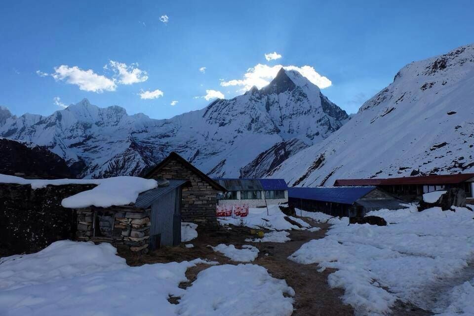 A snow-covered mountain landscape with a prominent peak, a stone building, and a blue-roofed structure.