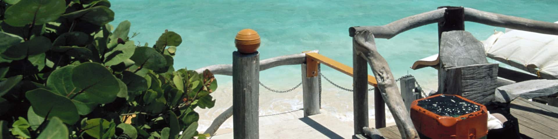 A wooden pier leading to turquoise waters with mountains in the background.