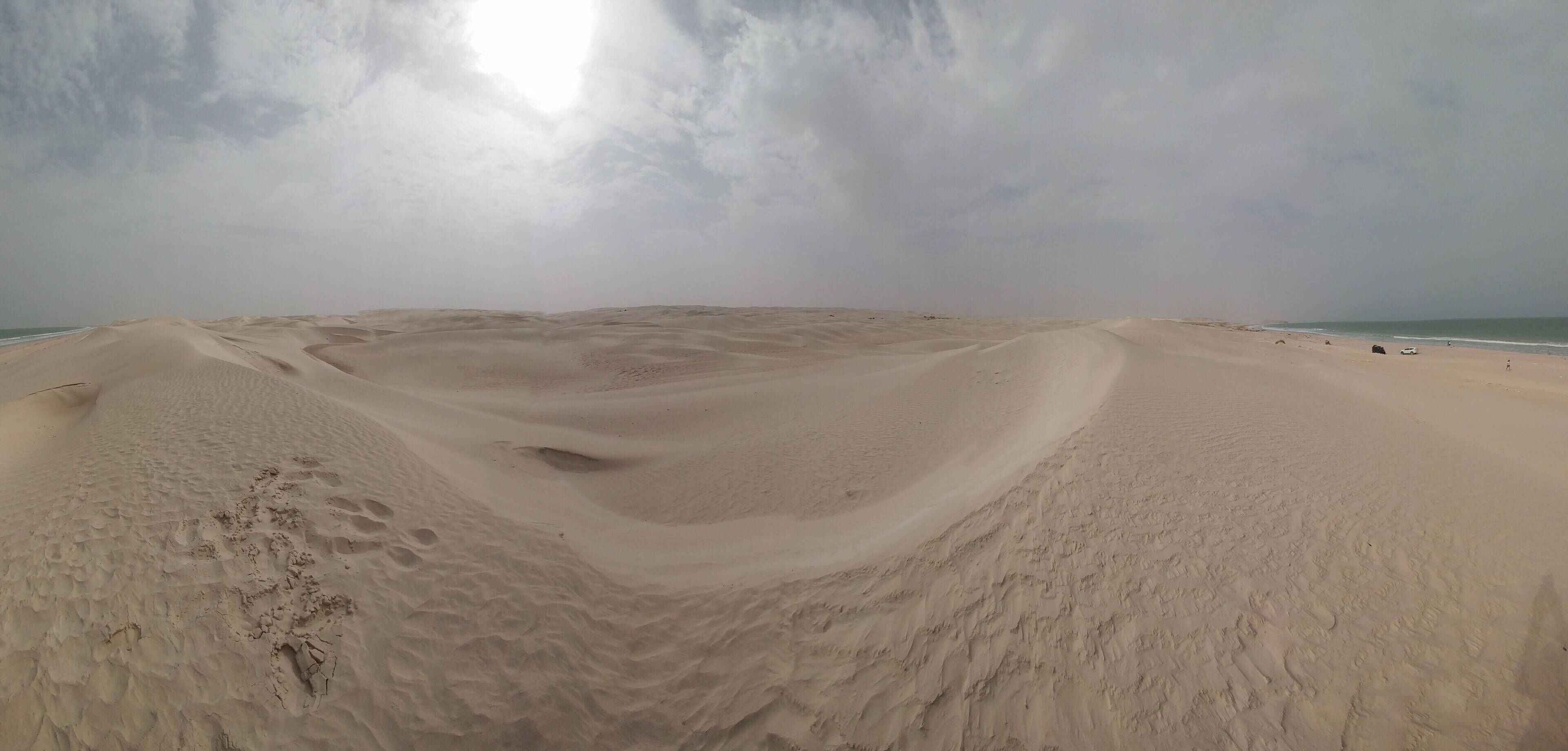 A desert landscape with a large sand dune and a beach in the distance.