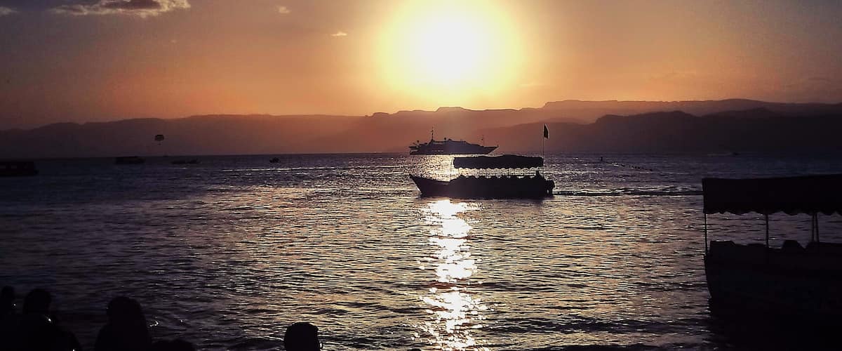 A sunset over a calm sea with a boat in the foreground and mountains in the background.