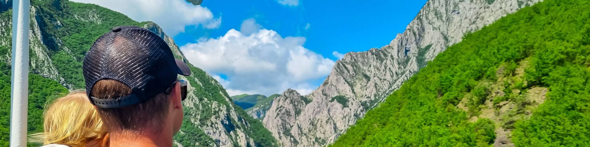Father holding baby on scenic ferry boat tour on Lake Koman reservoir on Drin river surrounded by forested steep hills, cliffs and mountain ranges of Albanian Alps. Panoramic view of Albanian Fjords