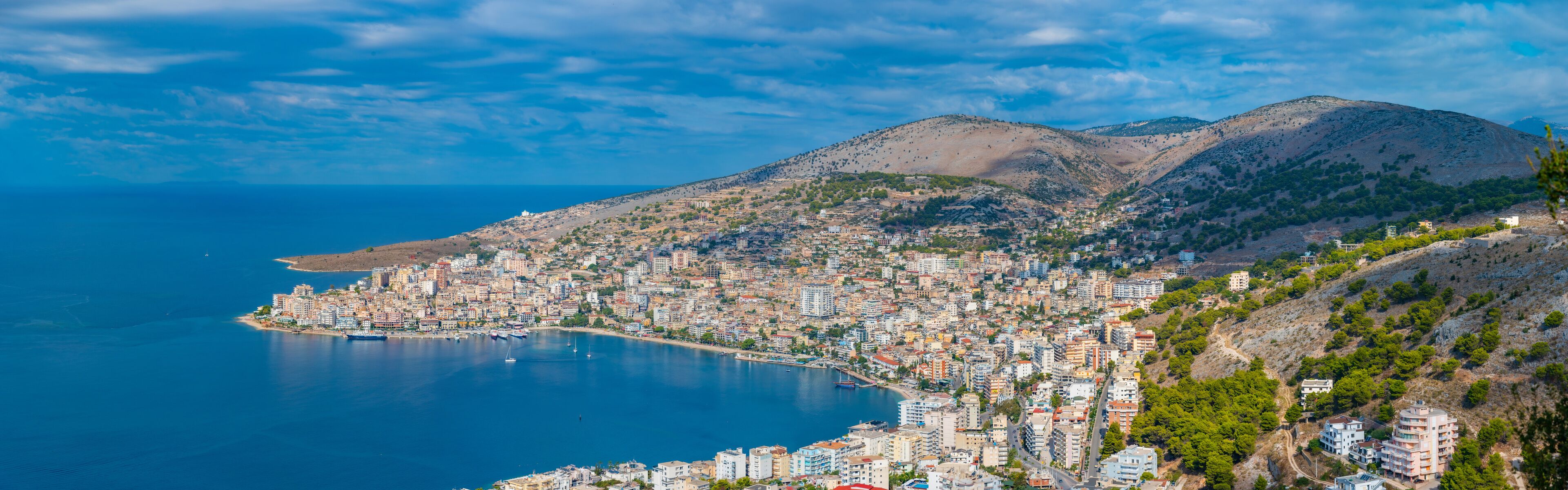 A coastal city with a dense urban area, a large body of water, and a mountainous backdrop.