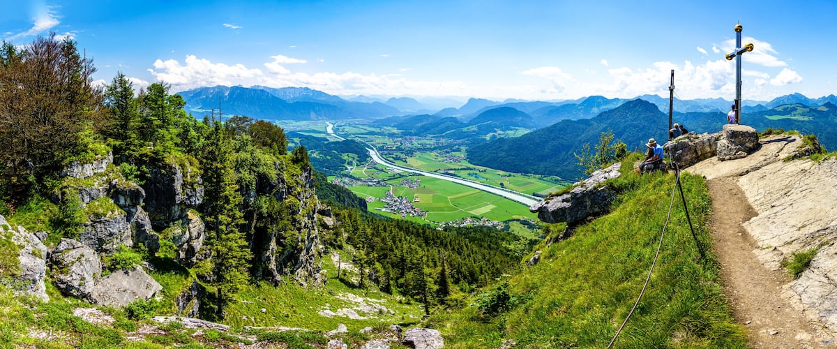 A mountainous landscape with a hiking trail, dense forests, and a distant village.
