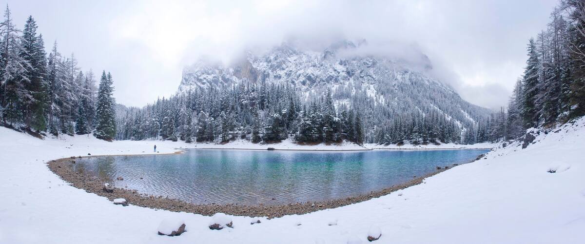 A snow-covered lake surrounded by dense forests and mountains.