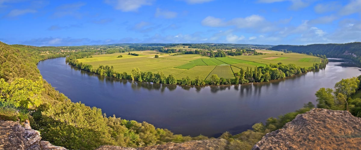 A river winding through a lush valley with fields and forests.