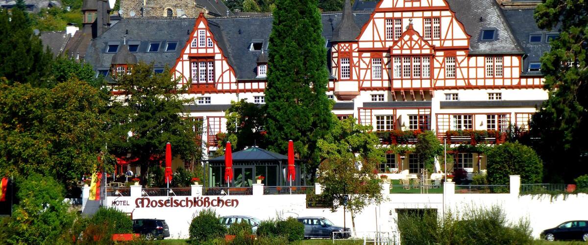 A traditional half-timbered building with a tower, surrounded by lush greenery and vineyards.