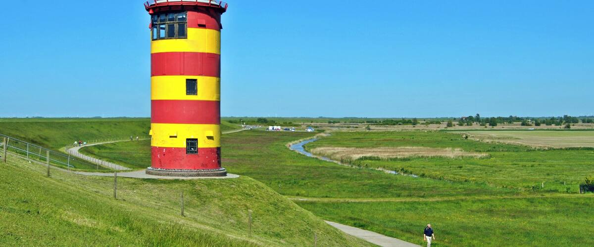 A tall lighthouse with red and yellow stripes, surrounded by green fields and a clear blue sky.