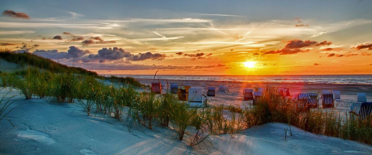 A beach at sunset with sand dunes, beach chairs, and the ocean.
