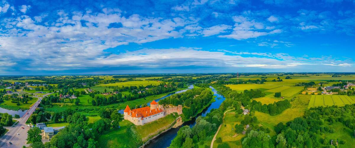 A castle surrounded by lush green fields, a river, and a clear blue sky.