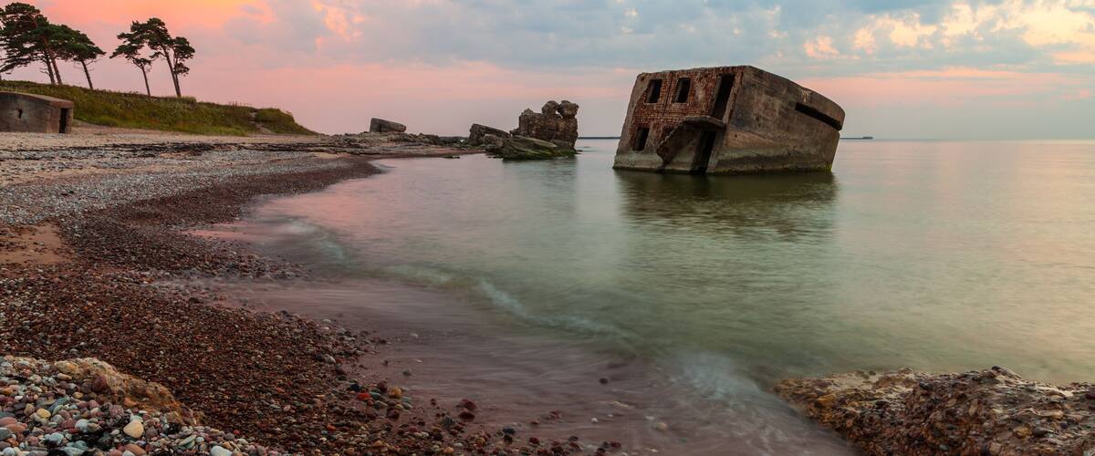 A rocky shoreline with a large shipwreck and trees in the background.