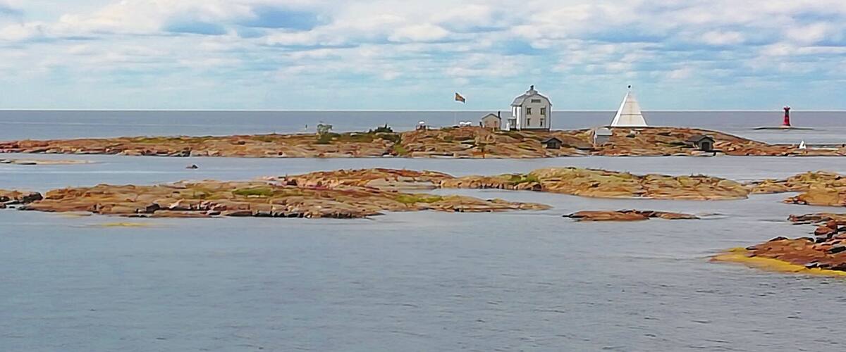 A coastal landscape with rocky outcrops, a lighthouse, and a white building.